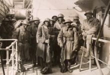 Men wearing military uniforms and holding long guns pose for a group photo aboard a ship.