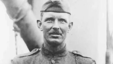 A man in a military dress uniform stands aboard a ship.