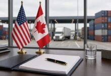 U.S. and Canadian flags beside an unsigned agreement, with a border crossing and shipping containers outside