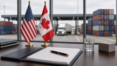 U.S. and Canadian flags beside an unsigned agreement, with a border crossing and shipping containers outside